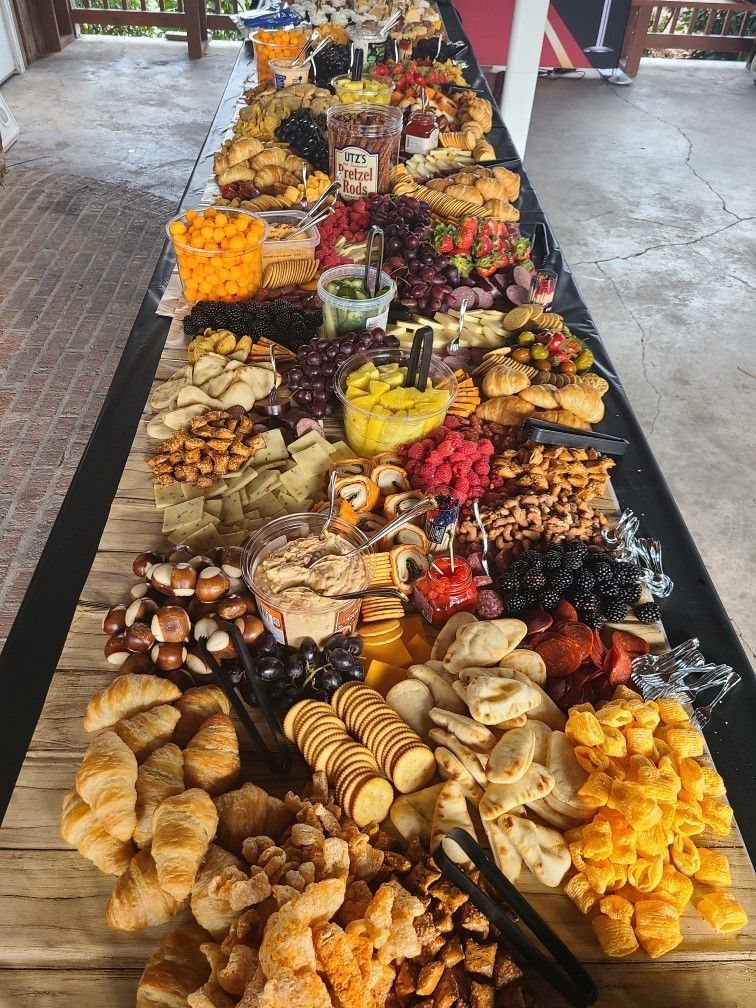 A long wooden table covered in a massive spread of charcuterie, cheeses, fruits, and breads.
