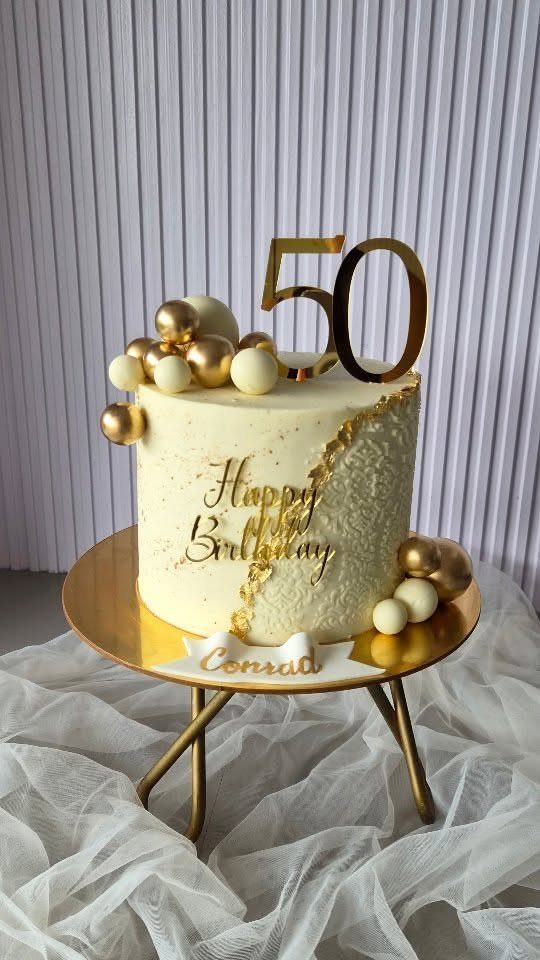 Cream birthday cake with gold decorations and a large gold number fifty topper.