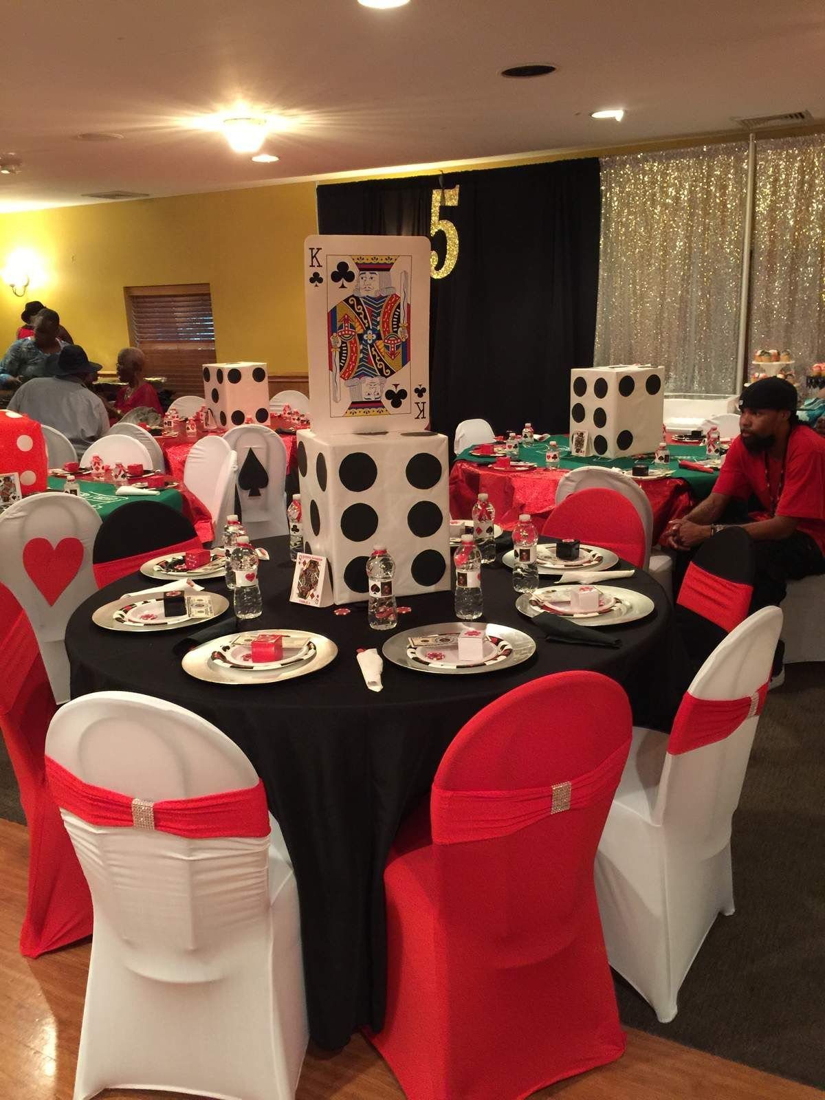 Decorated banquet tables with large dice and playing card centerpieces in a party venue.