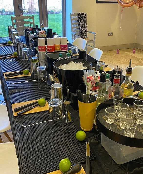 Cocktail making supplies including shakers, bottles, and limes arranged on a long black bar table.