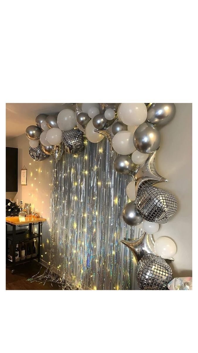 Silver and white balloon arch with disco balls over a shimmering tinsel curtain.