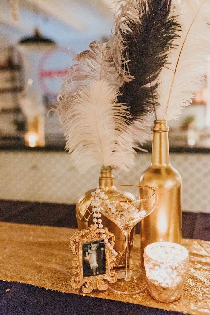 Gold centerpiece with black and white feathers, an ornate frame, and pearls on a sequin runner.