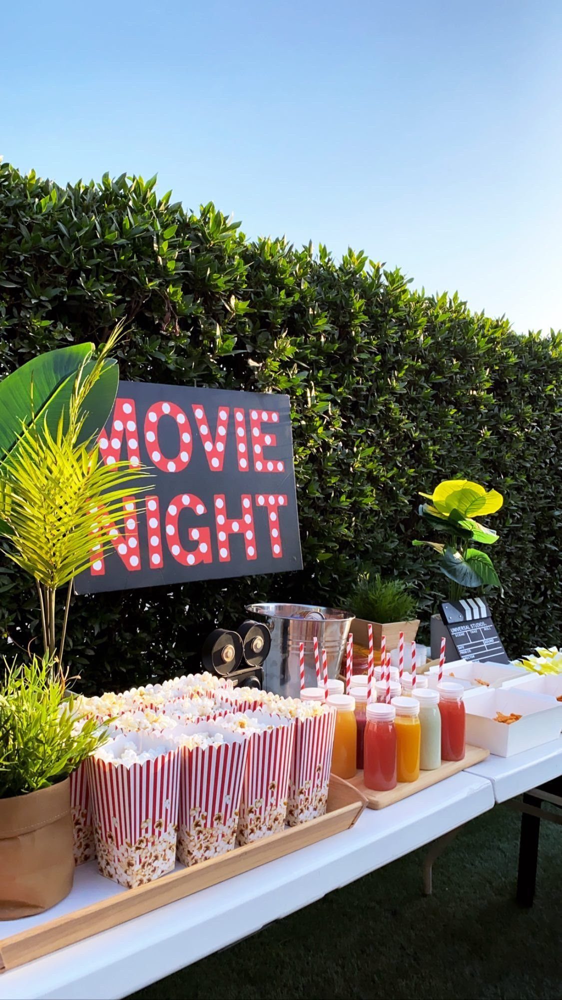 Popcorn containers and colorful drinks on a table with a glowing movie night sign.