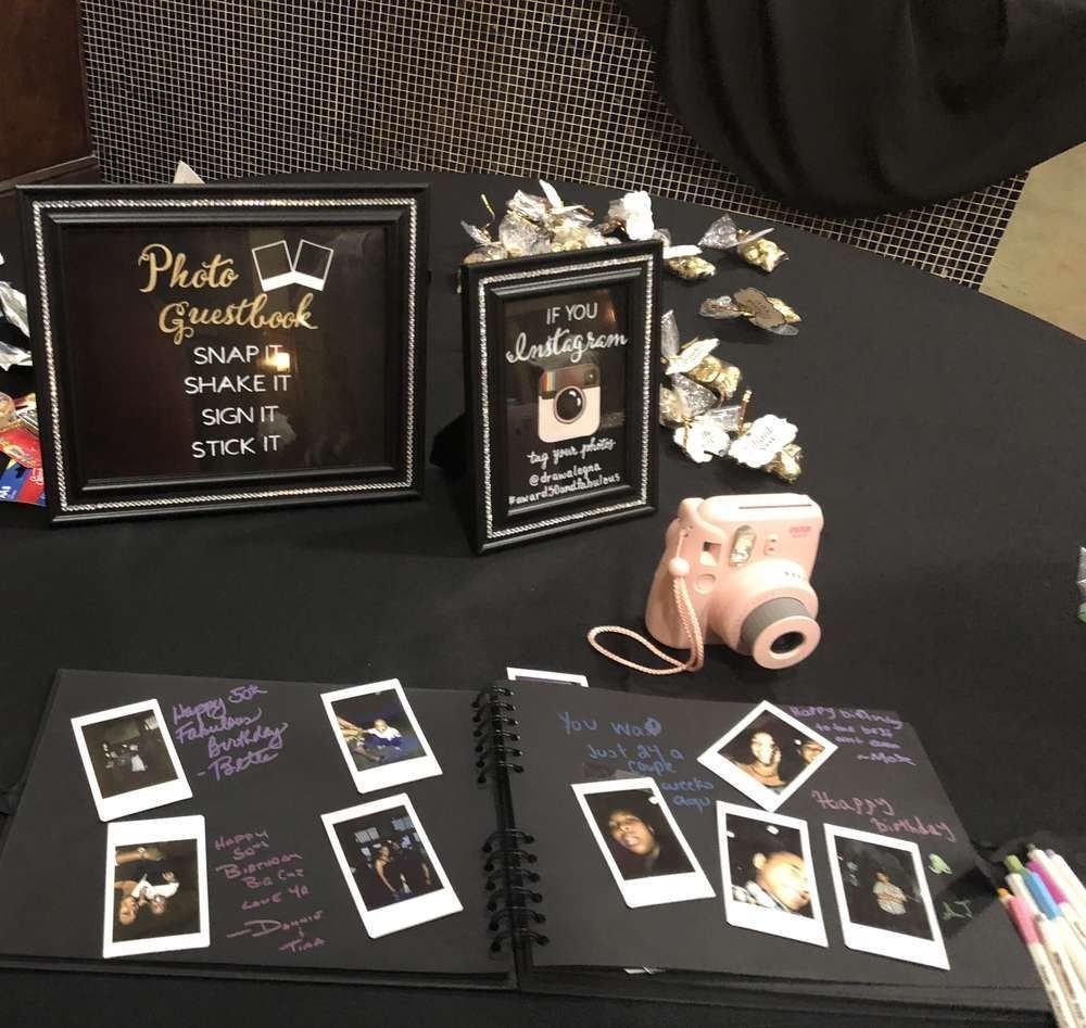 An open guestbook with polaroid photos and a pink instant camera on a black table.