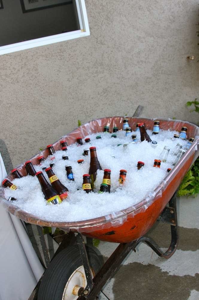 Beer bottles chilling in ice inside a red wheelbarrow outdoors.