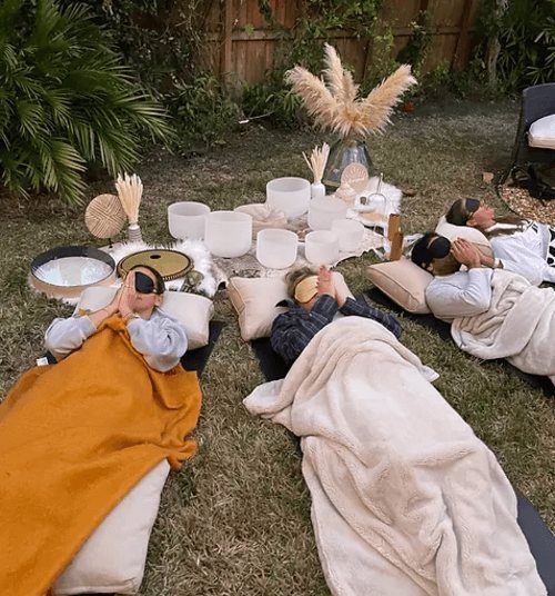 People lying on grass with eye masks and blankets during a wellness session.