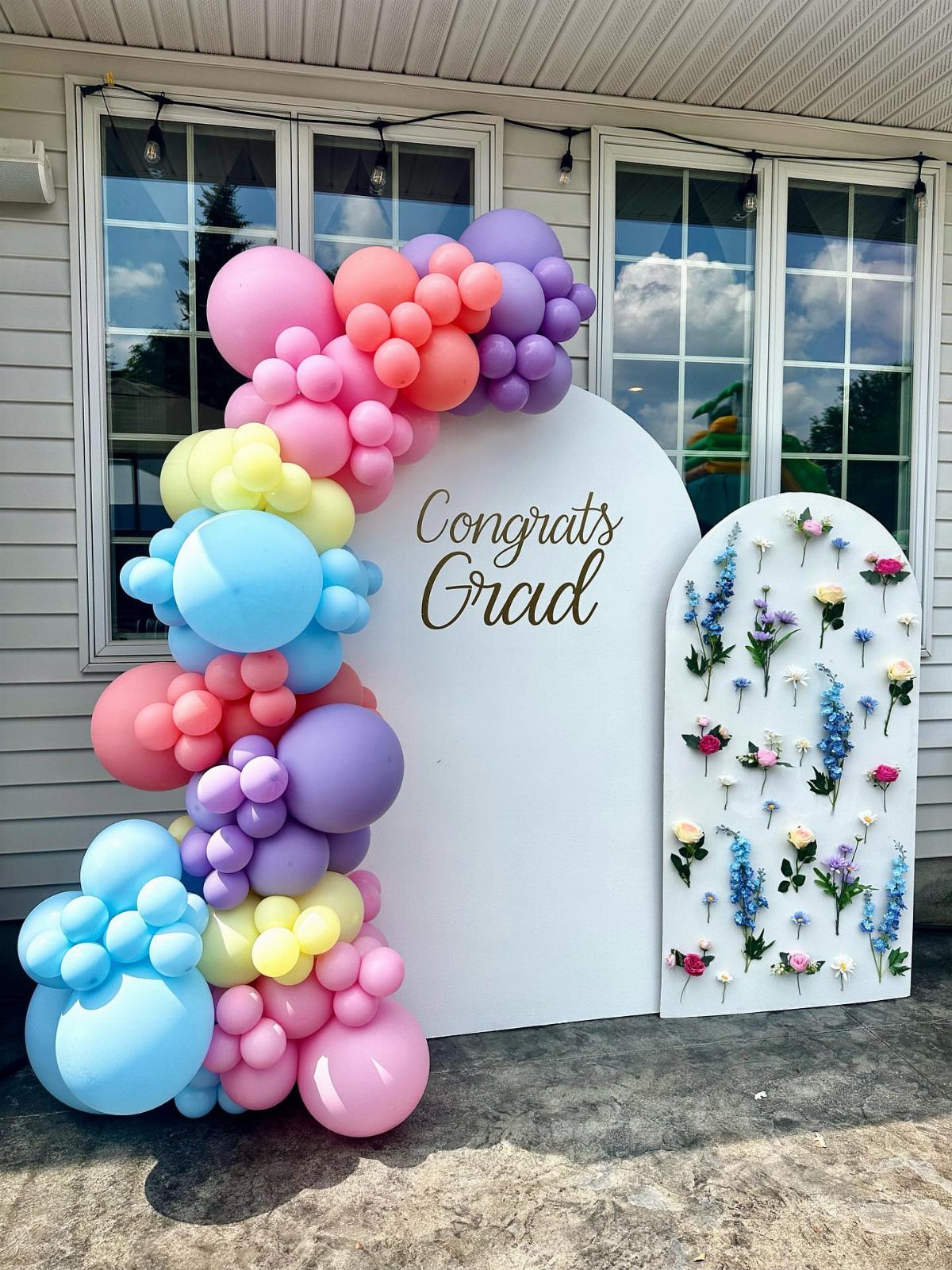 Pastel balloon arch framing a white backdrop with gold Congrats Grad text.