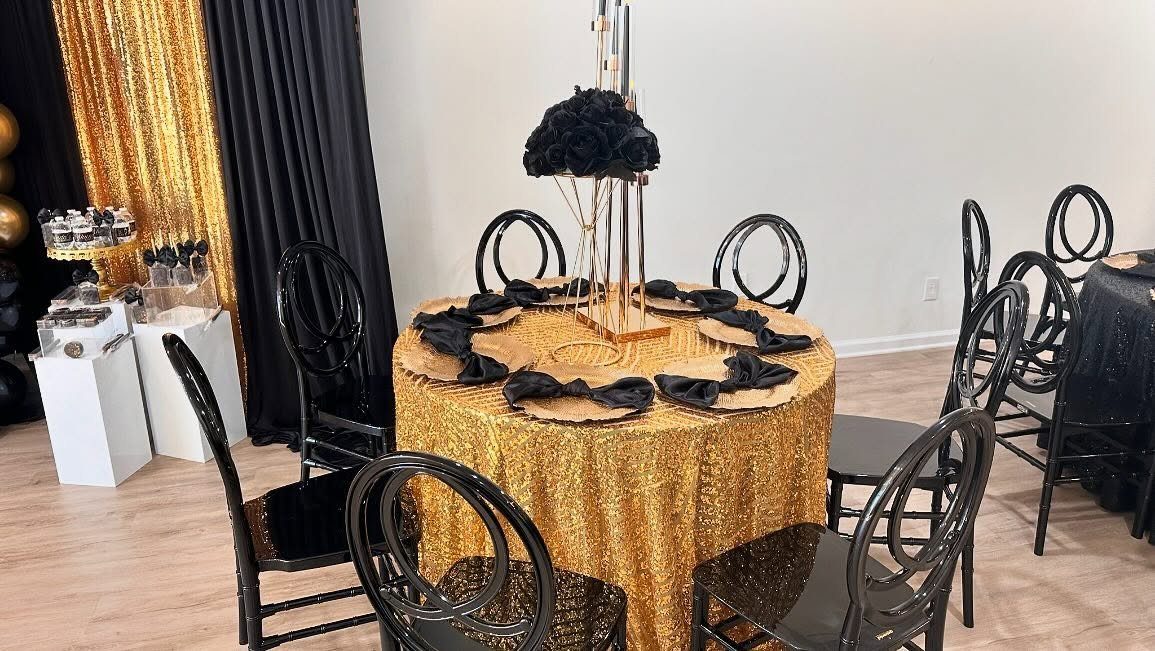 A round table with a gold sequin cloth, black napkins, and a tall black centerpiece.