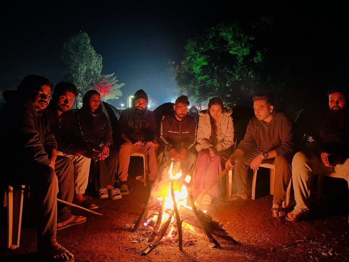 A group of people sitting in a circle around a glowing bonfire at night.