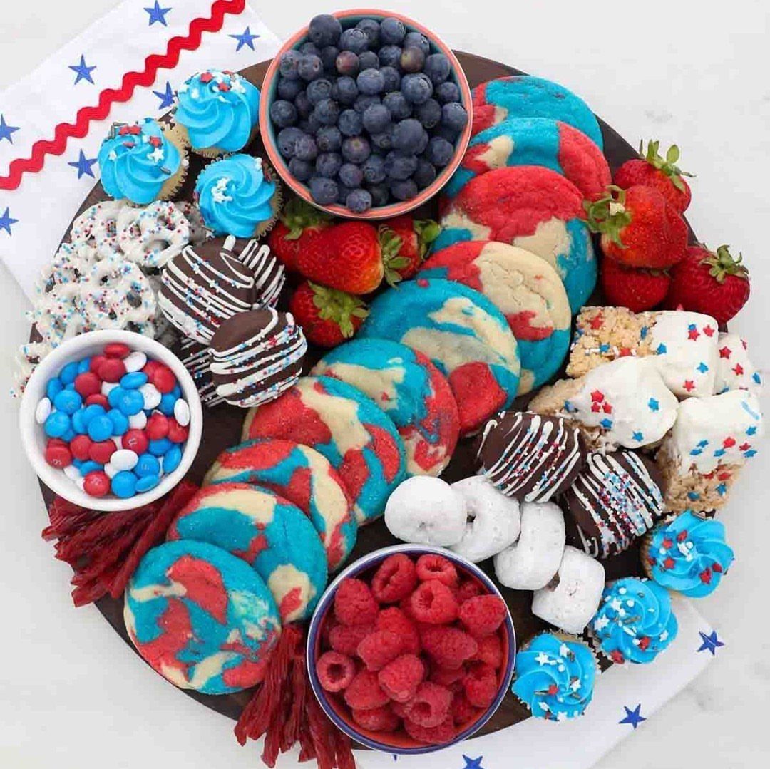 A dessert charcuterie board featuring red, white, and blue cookies, cupcakes, berries, and various sweet treats.