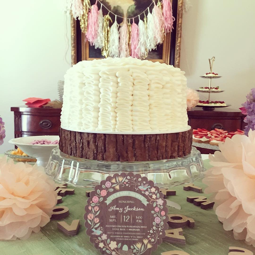 A white frosted cake on a glass stand with a floral invitation in front.