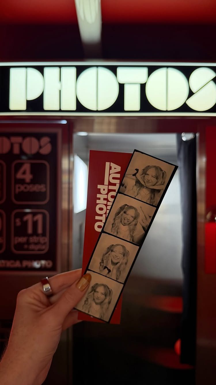 A hand holding two strips of black and white photo booth film strips in front of a machine.