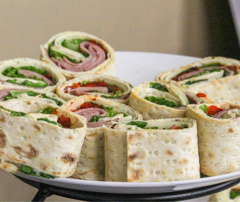 Sliced tortilla pinwheels filled with meat, spinach, and peppers on a white platter.