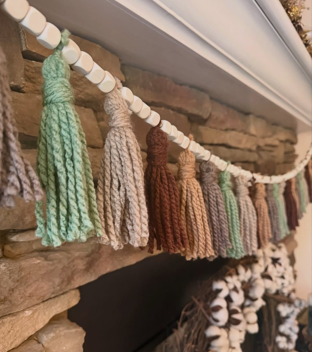A yarn tassel garland with white wooden beads hanging against a stone fireplace.