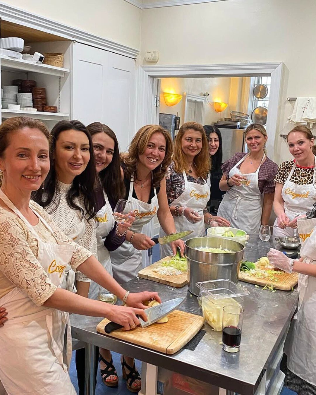 A group of women in white aprons smiling while preparing food in a kitchen.