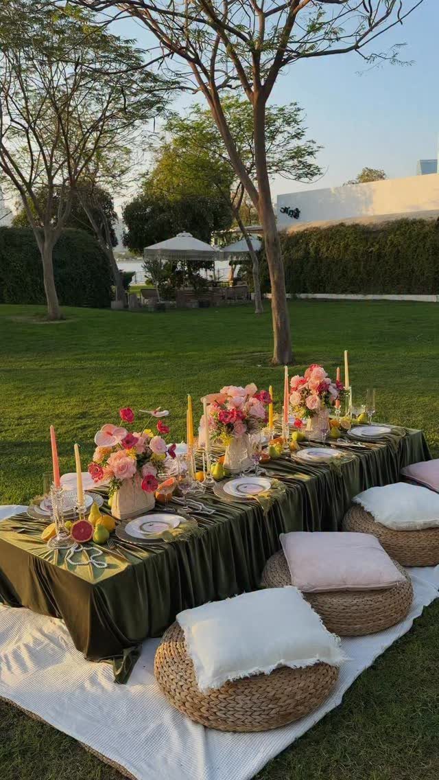 An elegant outdoor dining table set with flowers, candles, and floor cushions on a lawn.