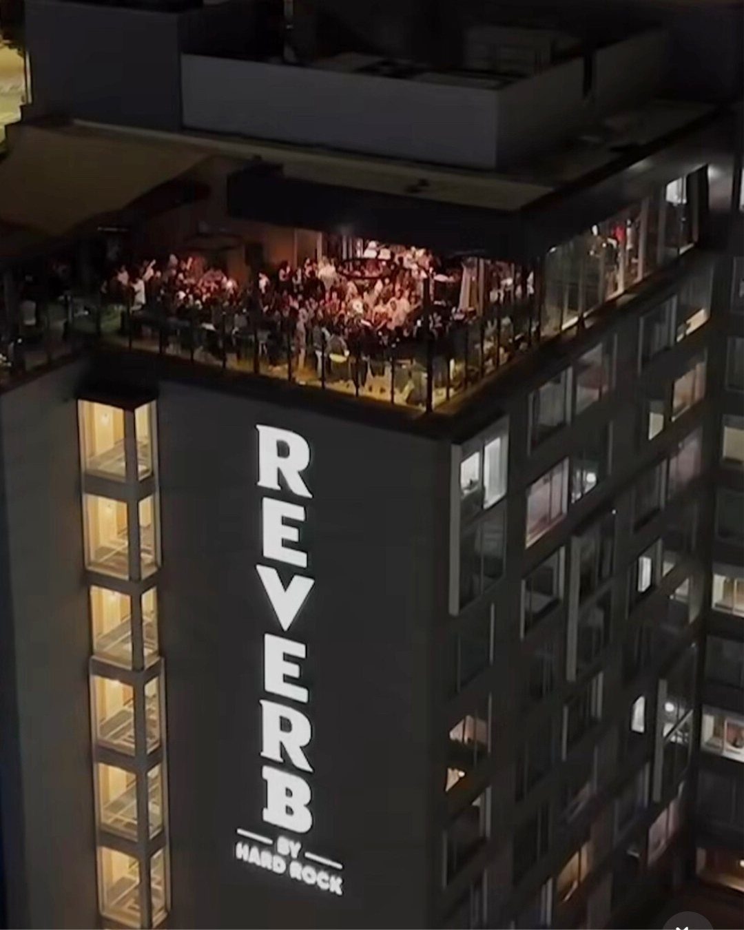 Crowd of people gathered on an illuminated rooftop bar at night.