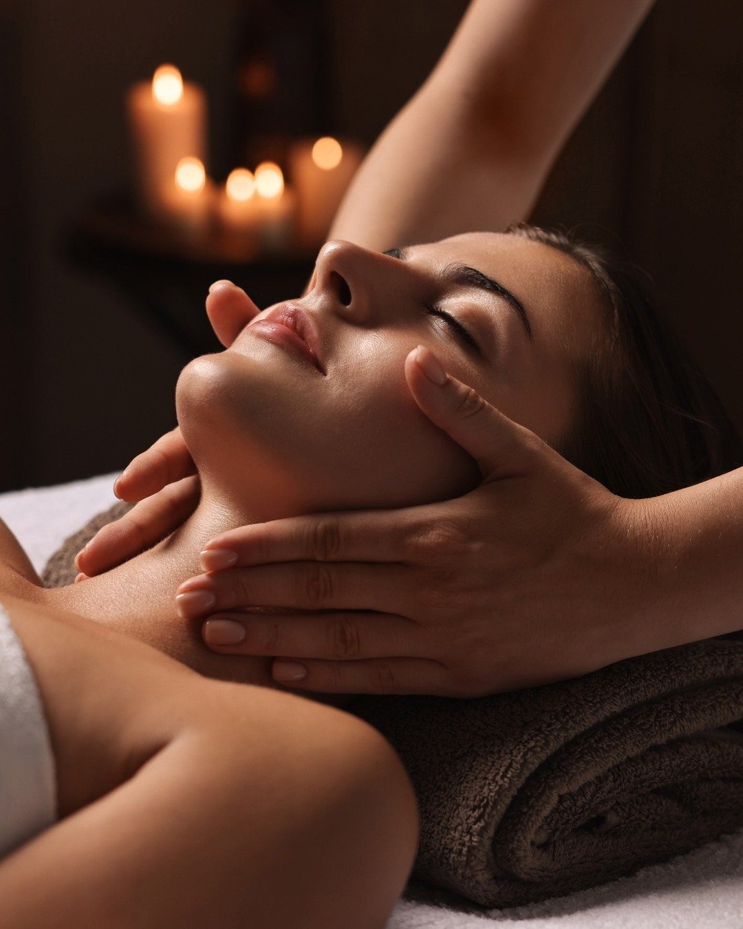 A woman receiving a relaxing facial massage with warm candlelight in the background.