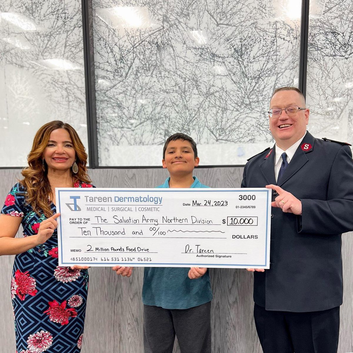 Three people smiling while holding a large ceremonial check for ten thousand dollars.