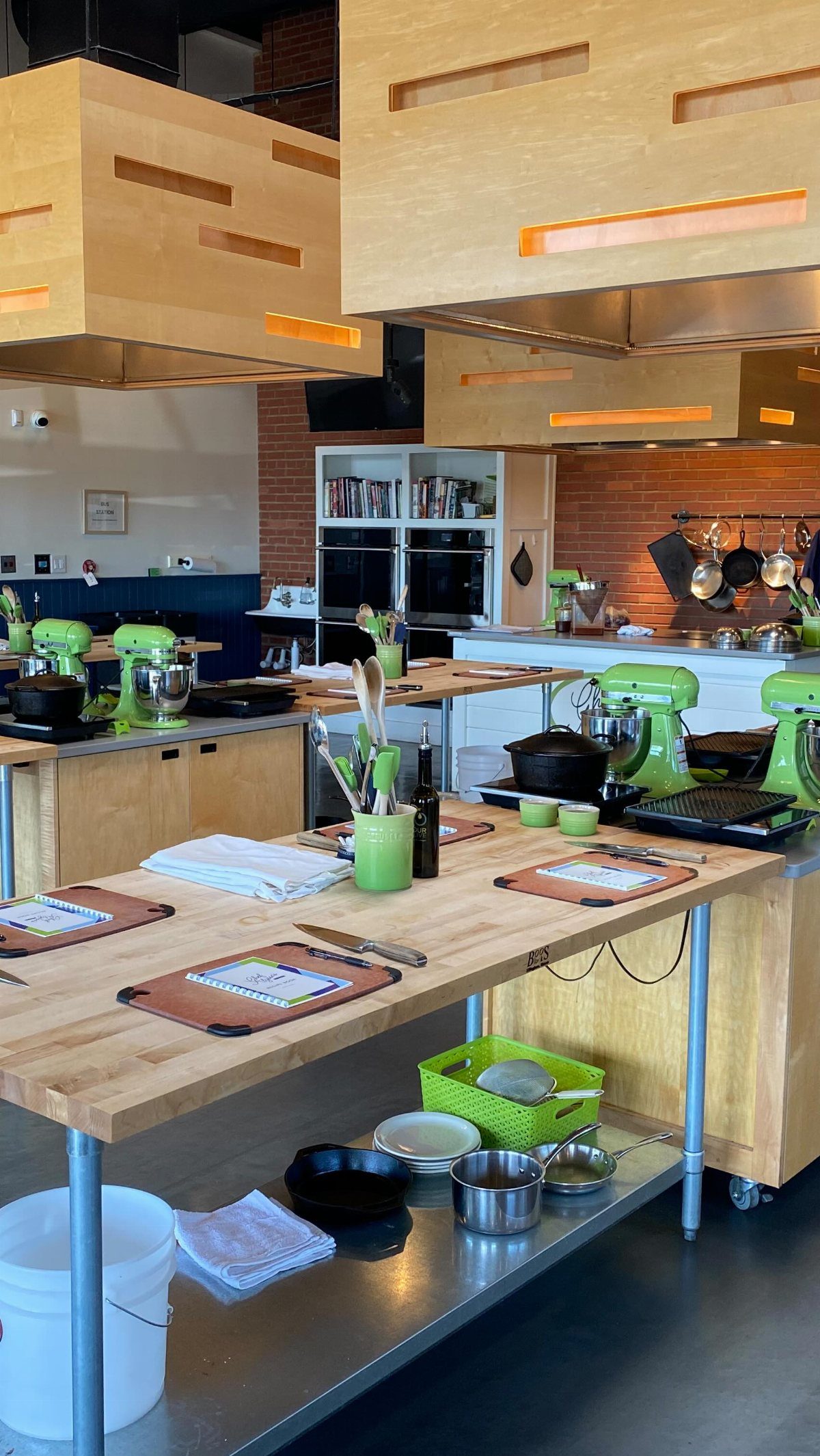 A professional kitchen setup with wooden tables, green stand mixers, and cooking supplies prepared for a class.