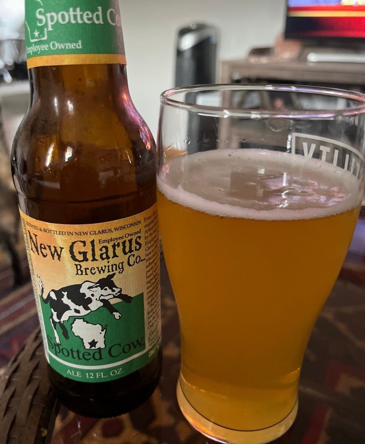 A bottle of Spotted Cow ale next to a full glass of golden beer.