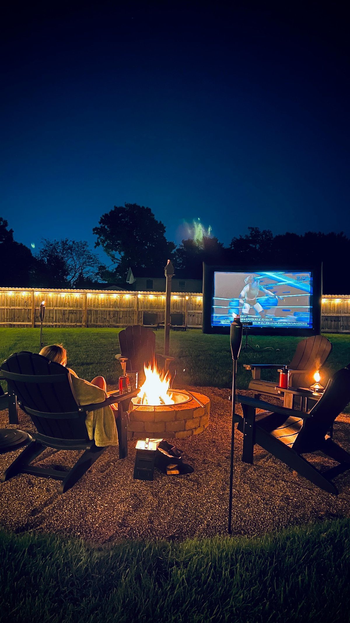 Outdoor movie screen and fire pit set up in a backyard at twilight.