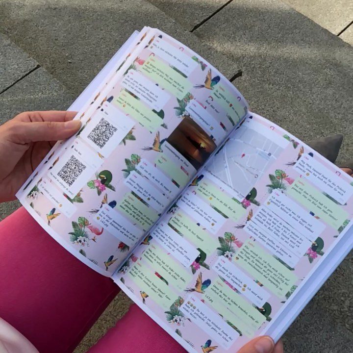 Hands holding an open scrapbook filled with colorful messages, photos, and floral designs.