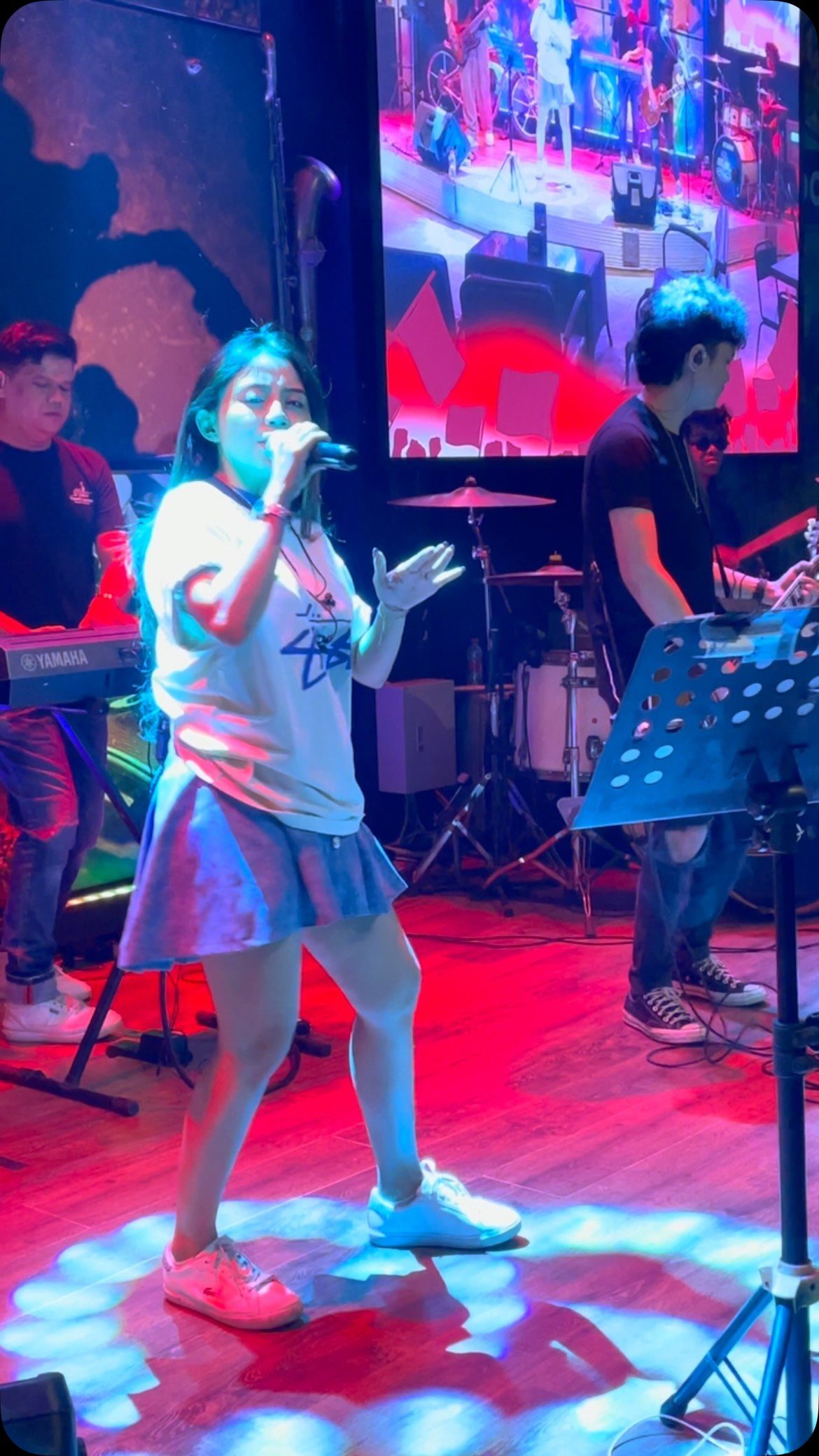 A female vocalist performing on a brightly lit stage with a band.