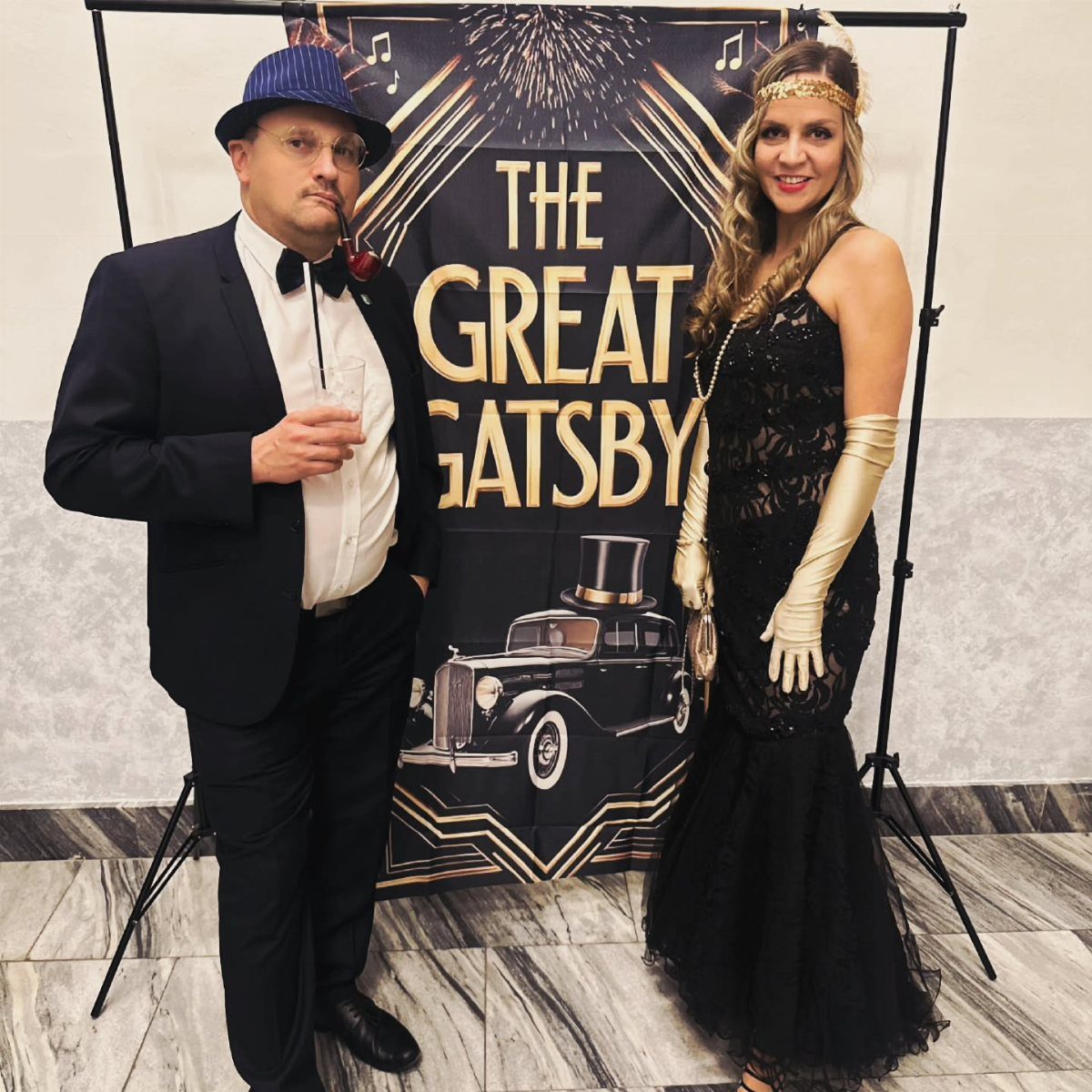A man in a suit and a woman in a Gatsby-style dress posing before a themed backdrop.