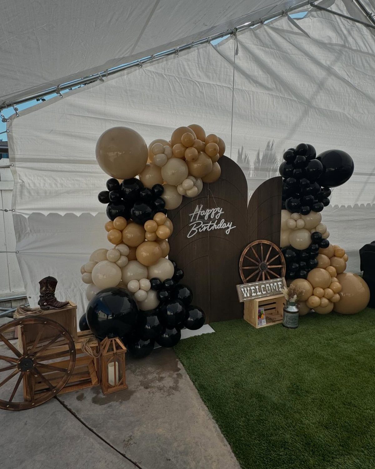 Western themed birthday decorations with balloon arches, wooden wheels, and a welcome sign under a tent.