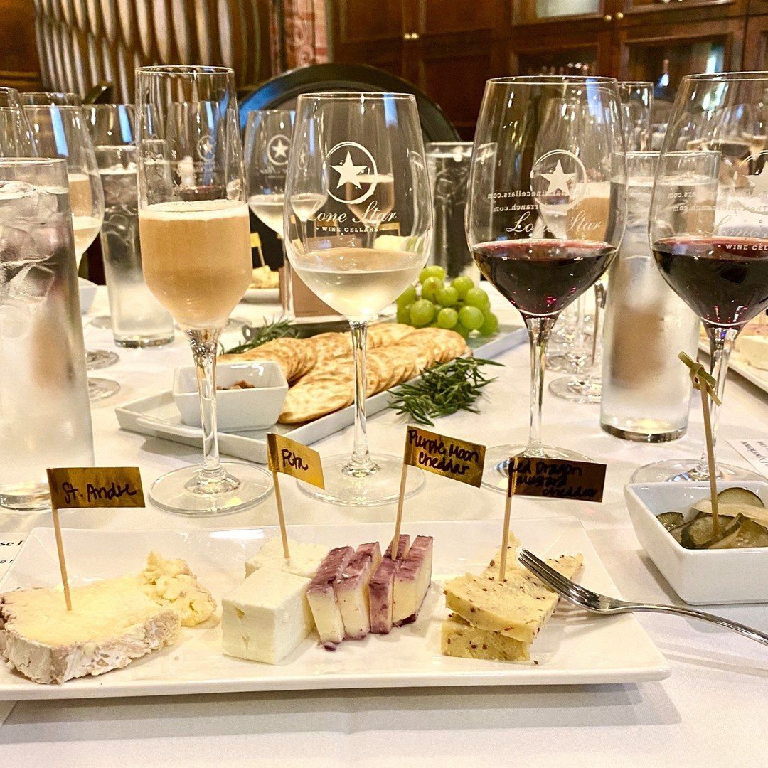 A wine and cheese tasting setup with various glasses, cheese platters, and grapes on a white table.