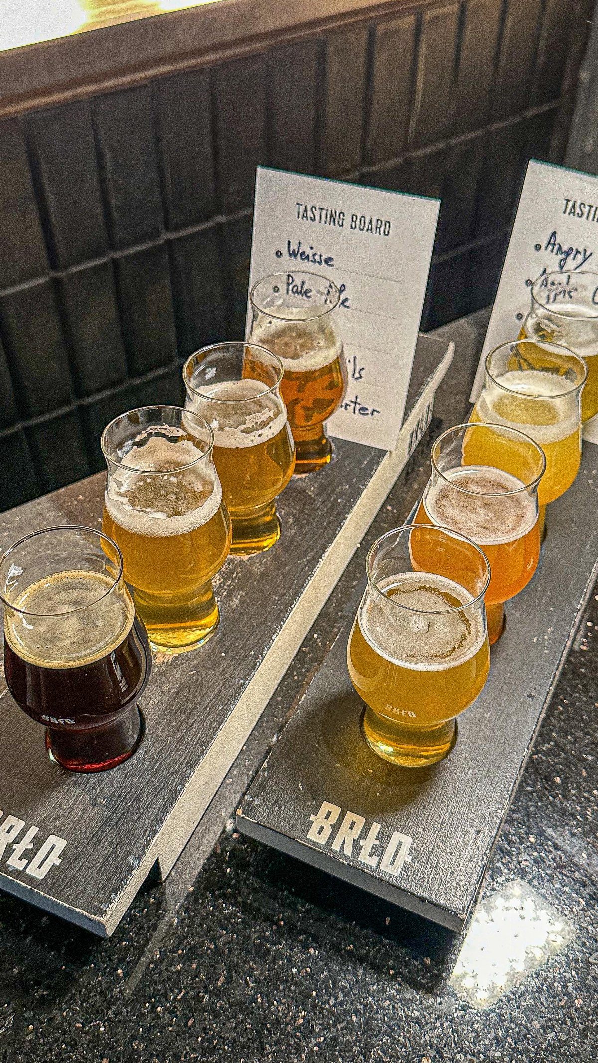 Craft beer tasting flight with various small glasses on wooden boards.