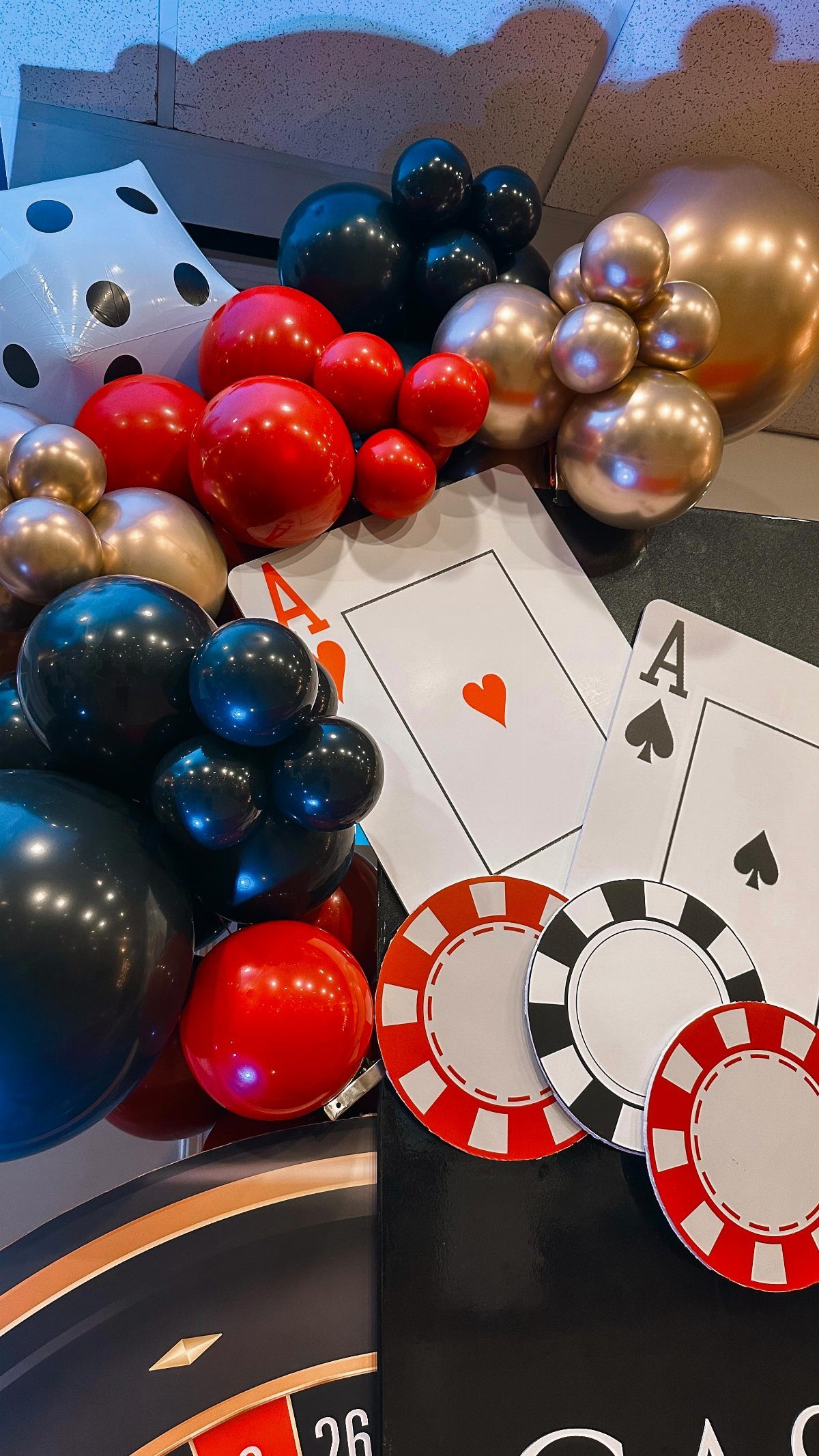 Casino themed decorations featuring balloons, playing cards, poker chips, and a large die.