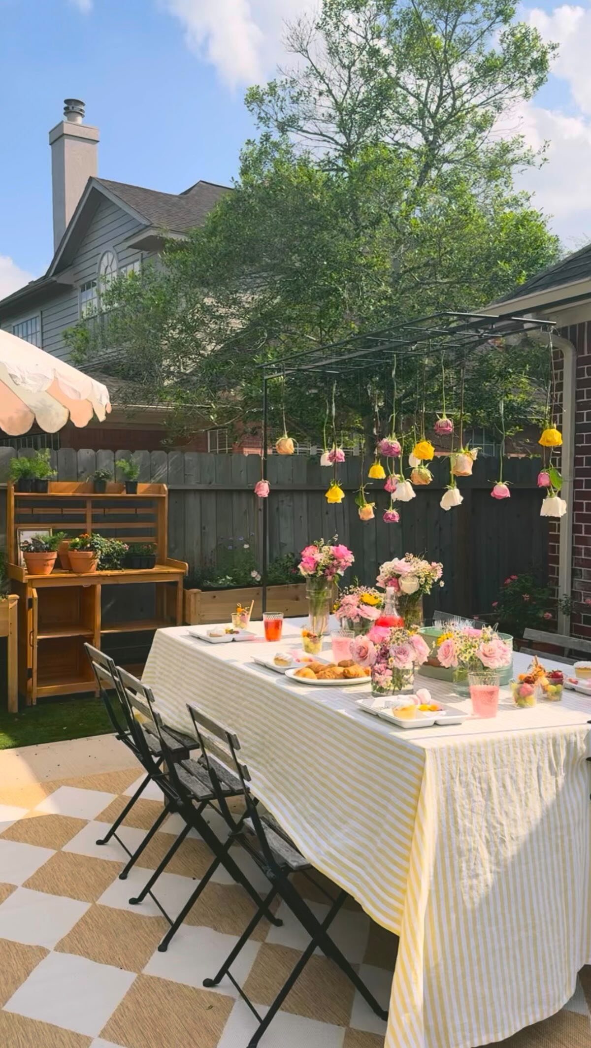 An elegantly set outdoor dining table with hanging flowers and pink floral centerpieces on a patio.