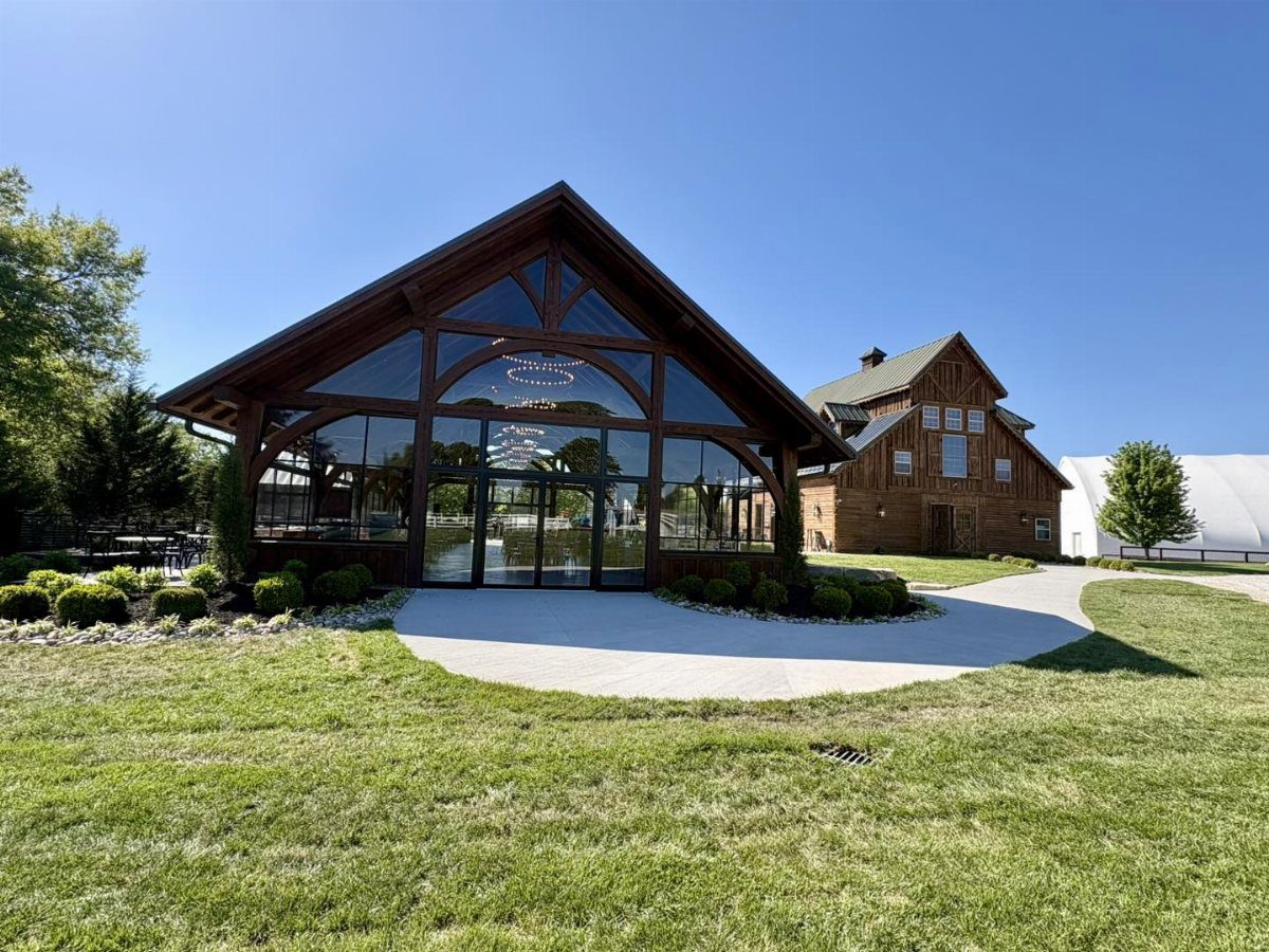 Large wooden pavilion with glass walls situated on a lush green lawn under a blue sky.