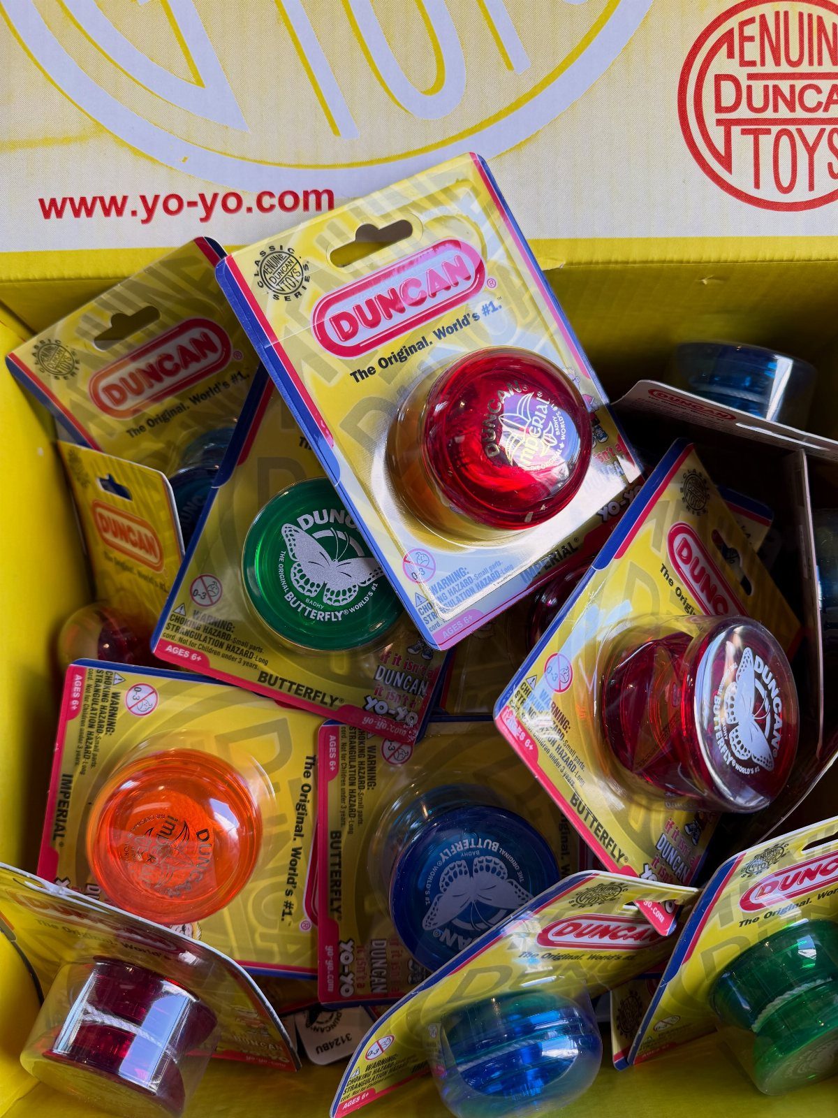 Multiple colorful Duncan brand yo-yos in their original retail packaging inside a yellow box.
