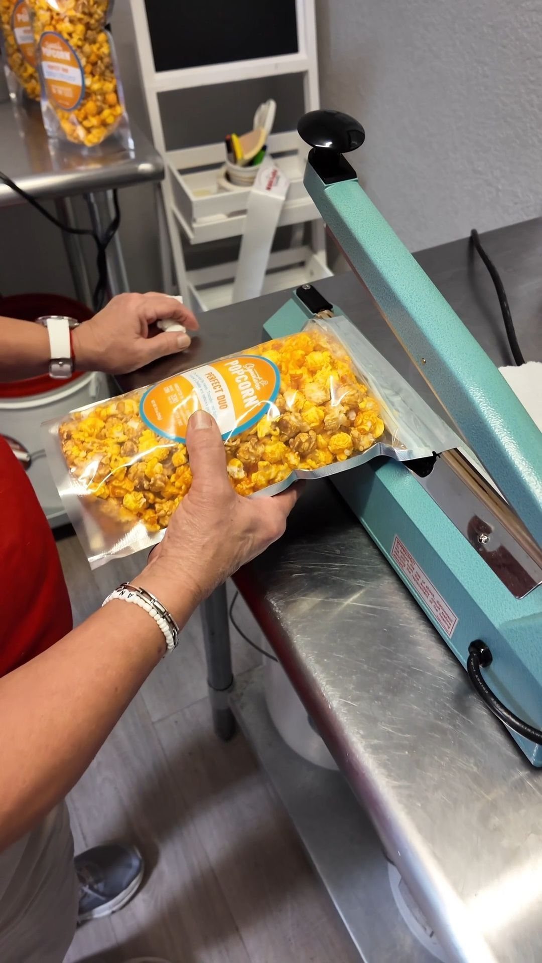 Hands holding a clear bag of yellow popcorn over a blue heat sealer machine.