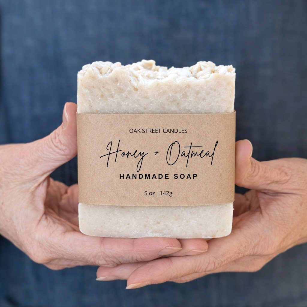 Hands holding a wrapped bar of honey and oatmeal handmade soap.