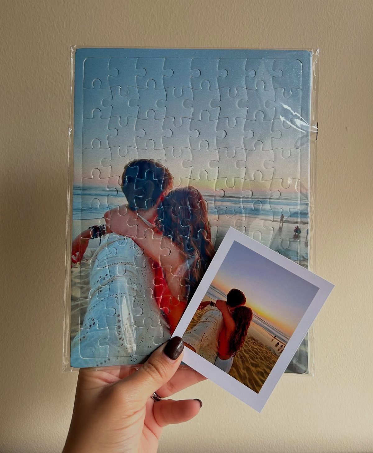 A hand holding a packaged jigsaw puzzle featuring a couple embracing on a beach at sunset.