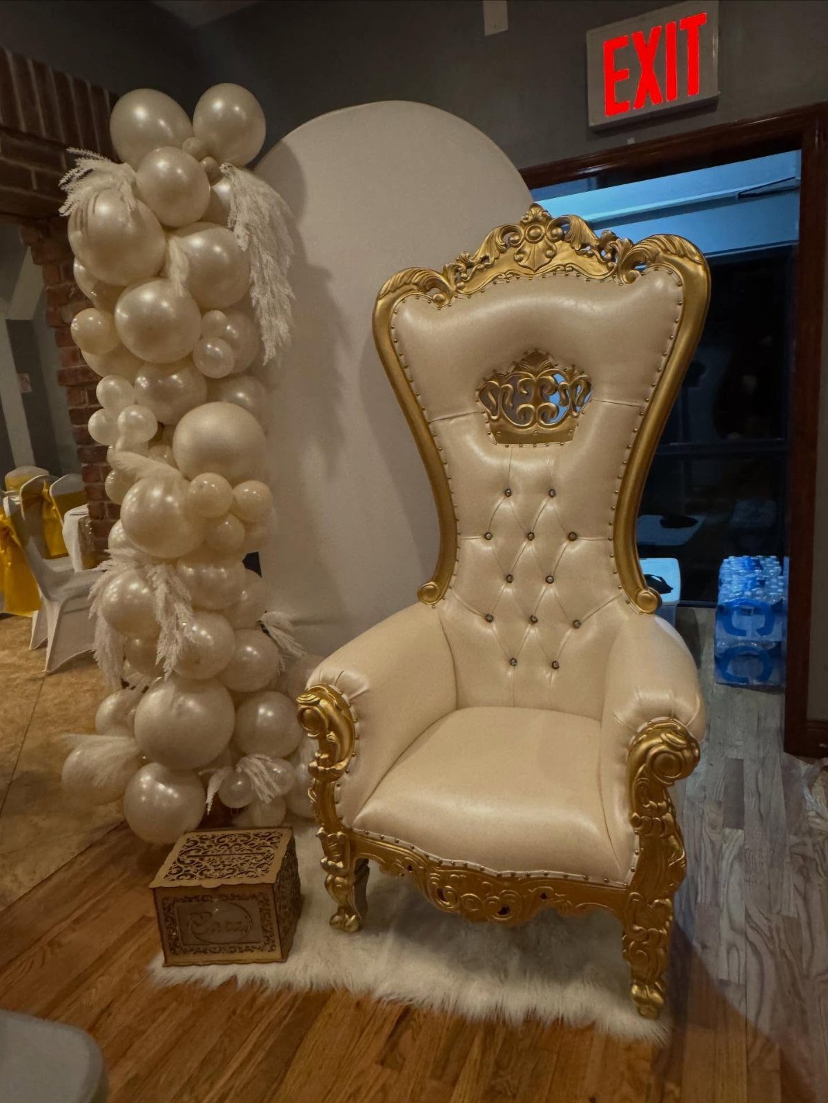 An ornate gold and cream throne chair next to a cream balloon arch.