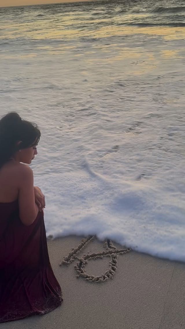 Woman in a red dress sitting on a beach next to the number 40 written in sand.