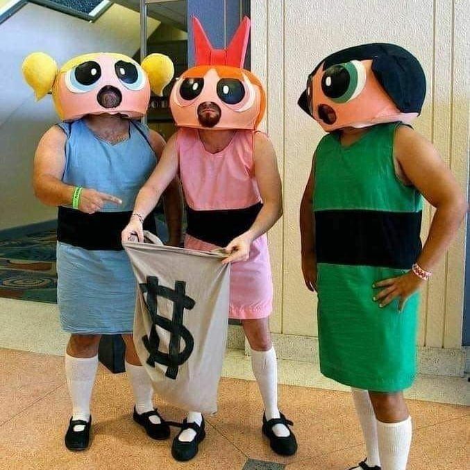 Three people wearing large character masks and colorful dresses holding a dollar sign banner.