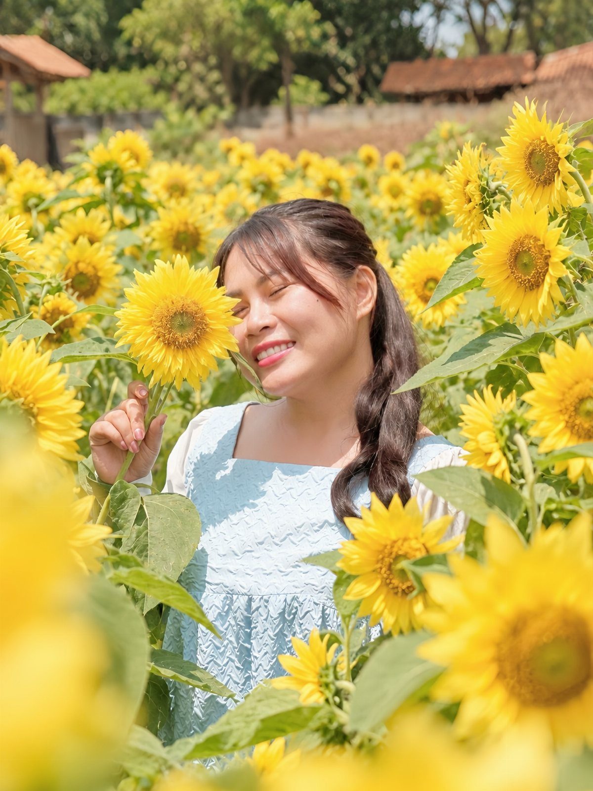 A smiling woman in a blue dress posing amidst a bright field of sunflowers.