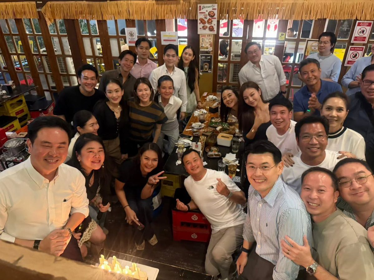 A large group of diverse friends smiling and posing closely together around a dining table.