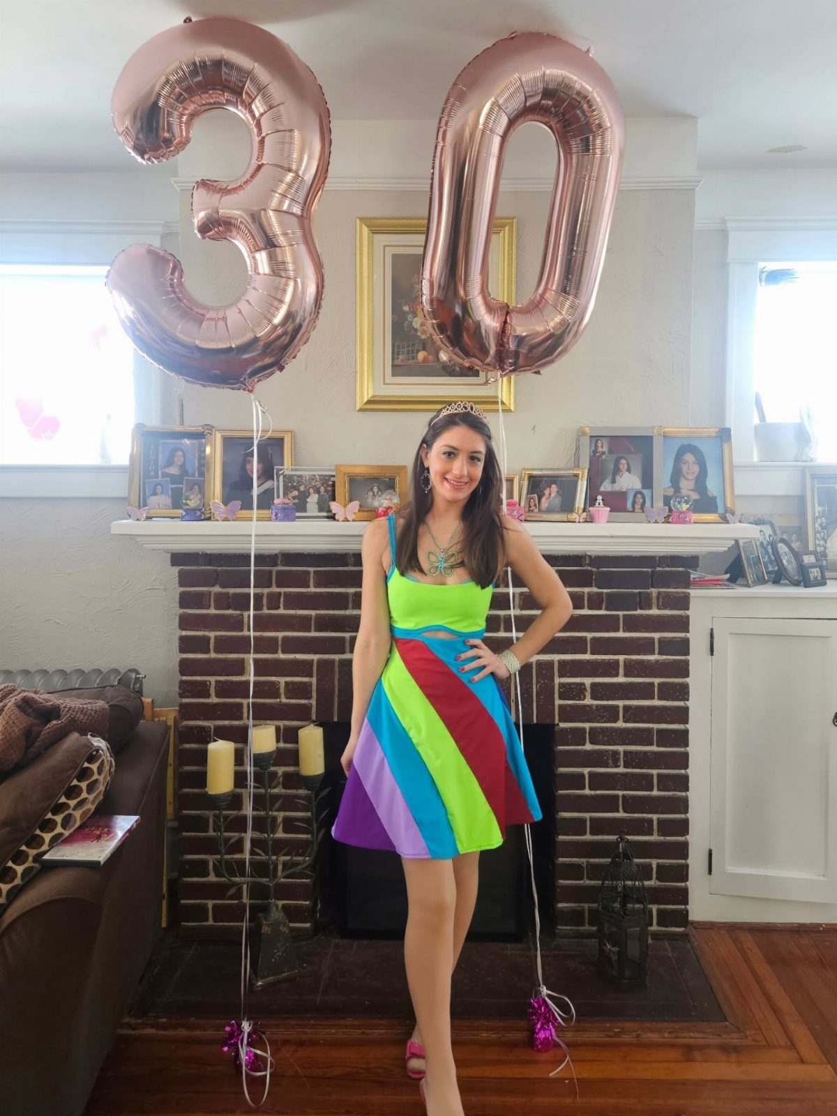 A woman in a colorful striped dress posing with large rose gold number 30 balloons.