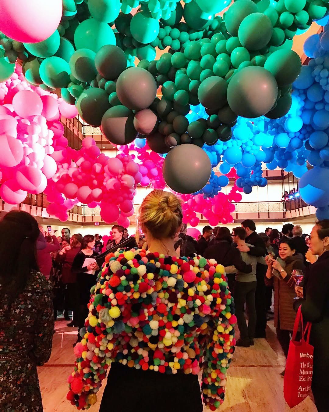 Vibrant pink, teal, and blue balloons hanging in large clusters over a crowd of people.