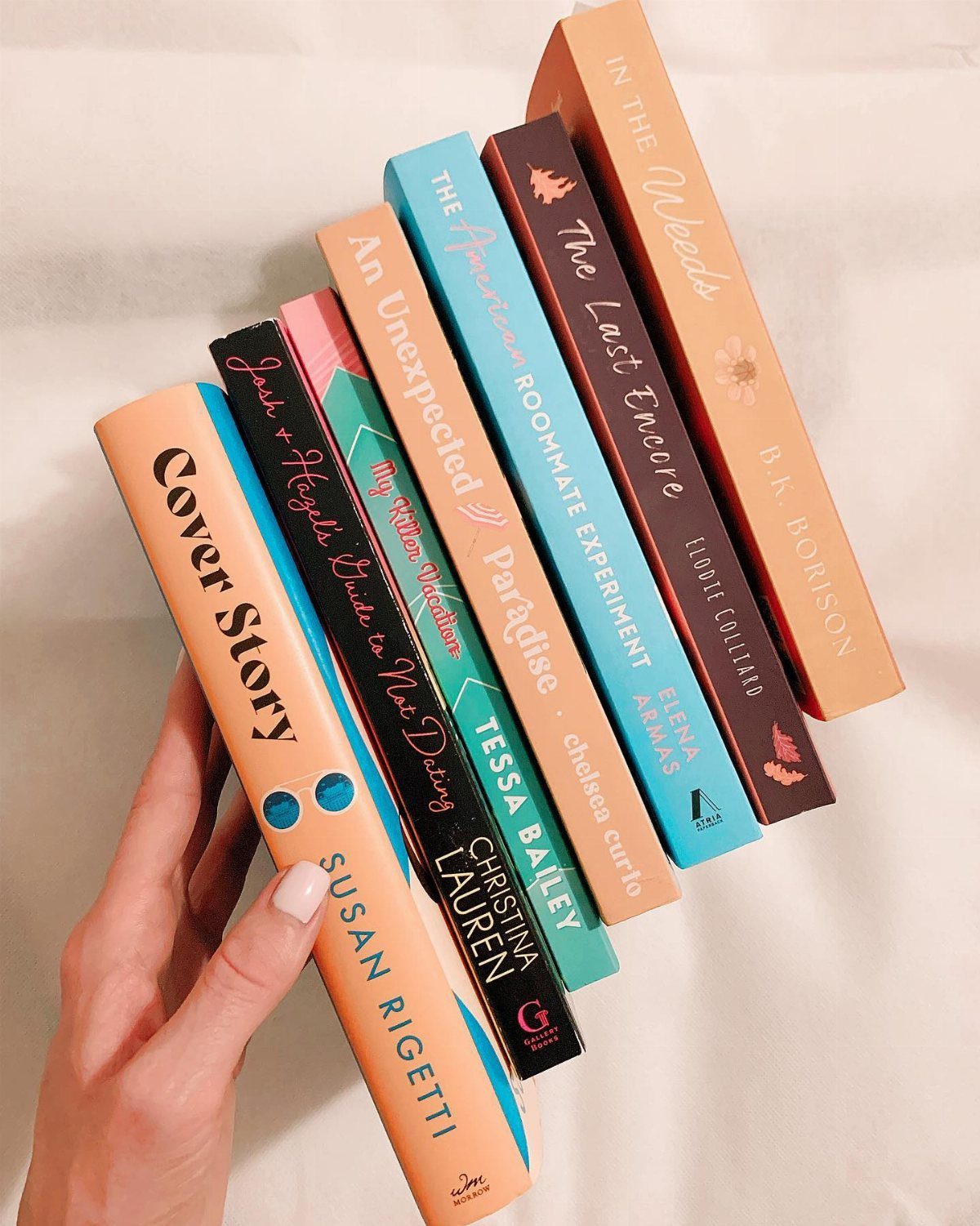 A hand holding a colorful fan of various book spines against a white background.