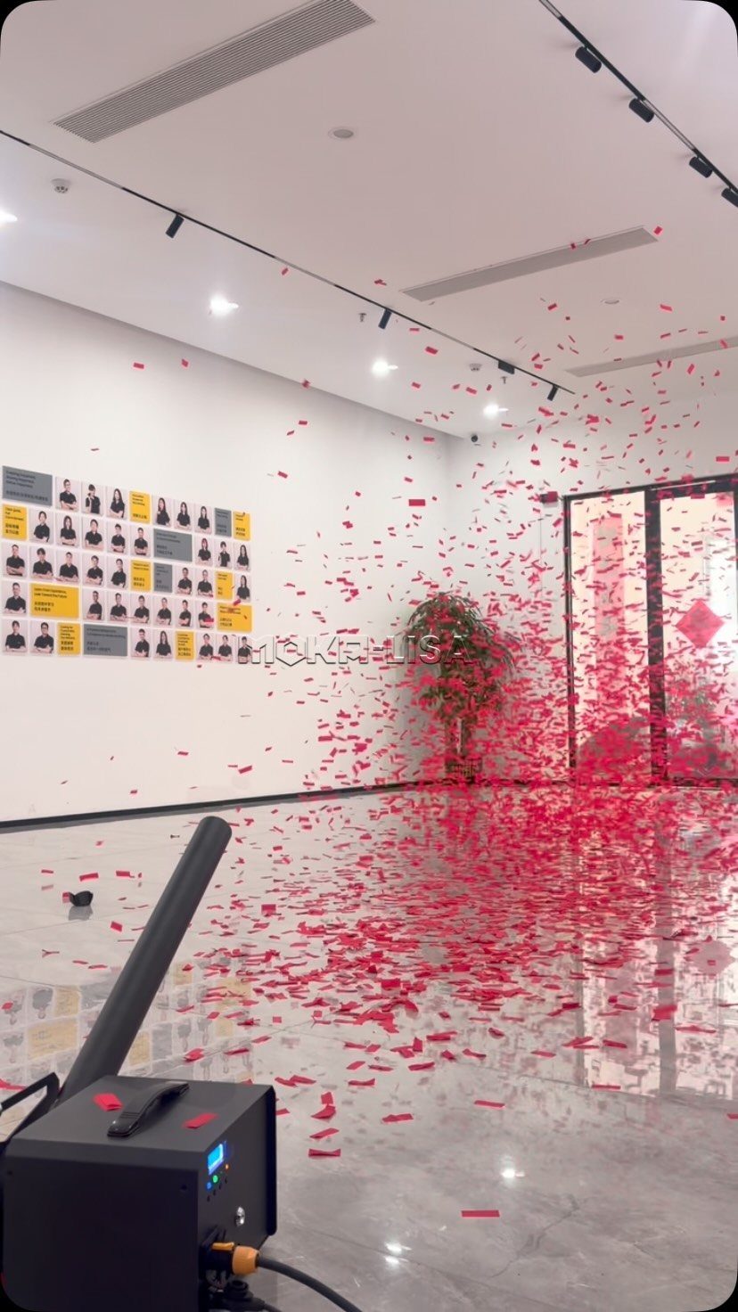 Red confetti exploding from a machine across a bright, modern white room.