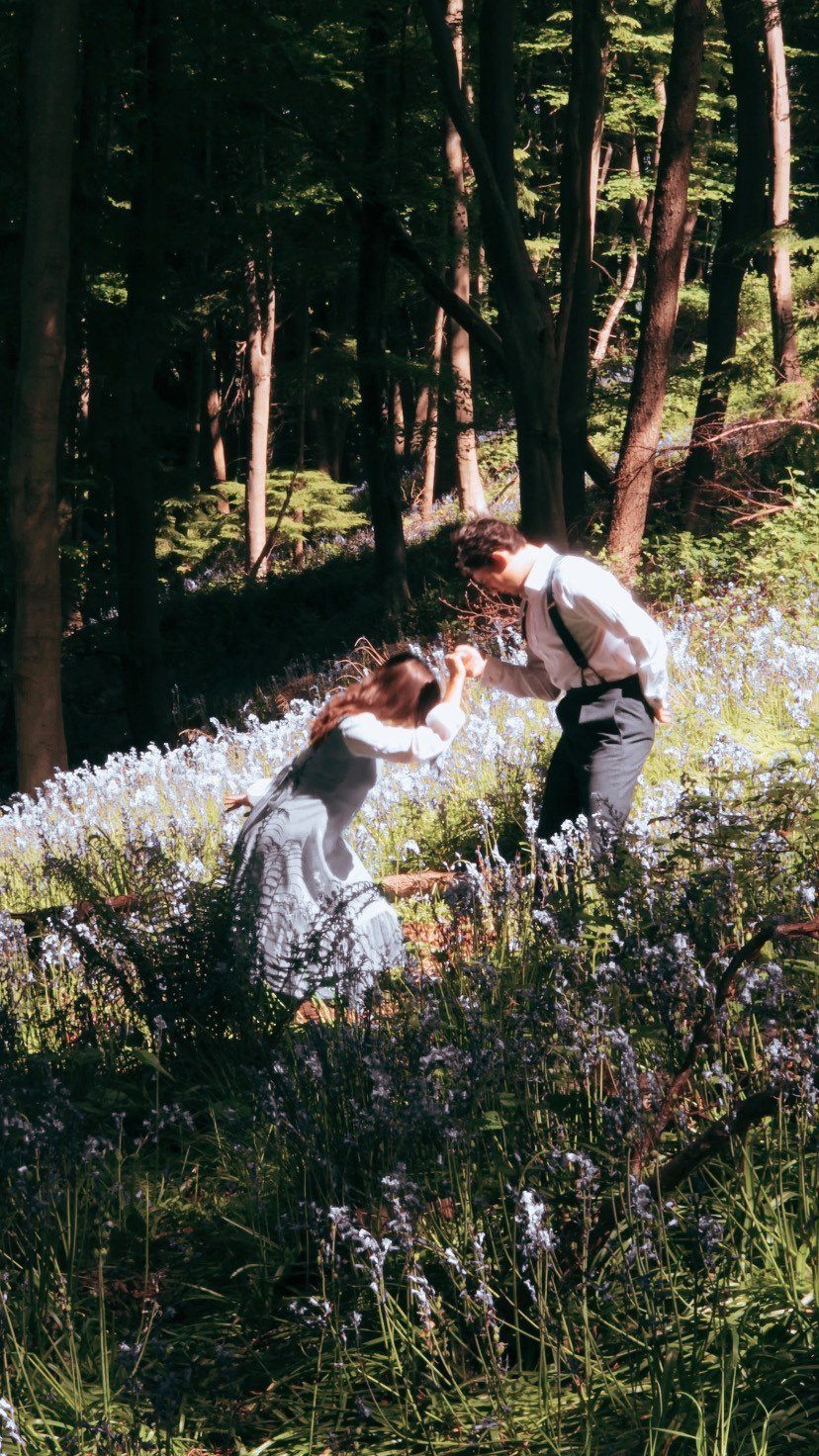 A couple dancing in a sunlit forest clearing filled with blue wildflowers.