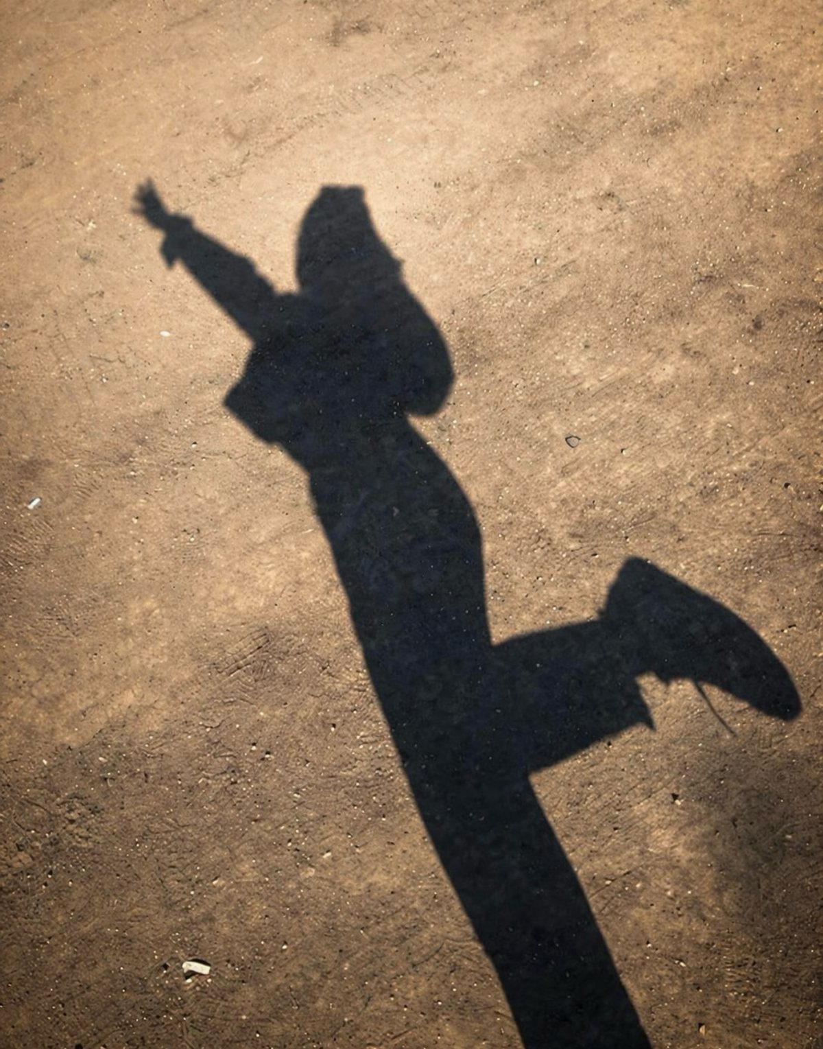 Shadow of a person posing with one arm raised on sandy ground.